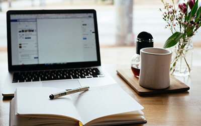 A laptop, notebook, and cup of coffee on a table.