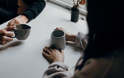 Two people sitting at a table both holding coffee mugs.