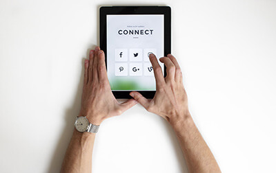 Hands holding a tablet while looking at links to different social media sites.